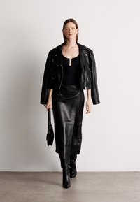 Musta nahkainen moottoripyörätakki, tiukka musta toppi ja pitkä nahkahame, yhdistettynä polven yli ulottuviin mustiin saappaisiin ja pieneen käsilaukkuun.