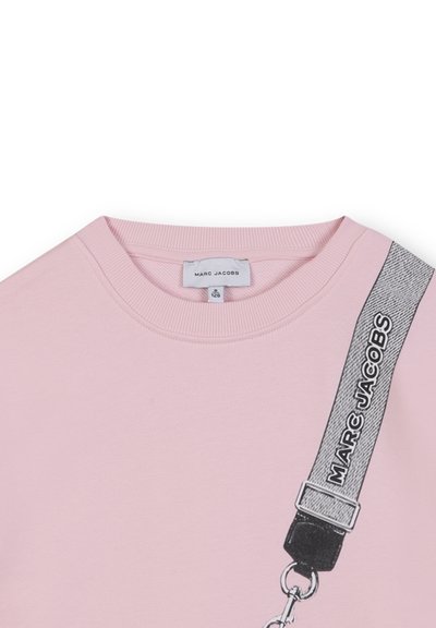 Sweatshirt rose clair avec un col rond, présentant une sangle noire avec le texte "MARC JACOBS" et un détail de fermoir en métal. Texture douce.