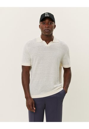 Polo shirt à manches courtes de couleur claire avec un décolleté en V, un col côtelé et des poignets. Le tissu semble doux avec une finition légèrement texturée.