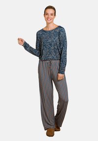 Bloemige lange mouw top in nachtblauw met een losse fitting, gecombineerd met gestreepte wijde broek in blauw, crème en roest; comfortabele bruine schoeisel.