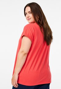 Koraal kleurig T-shirt met korte mouwen en een ontspannen pasvorm, met opgerolde mouwen, gemaakt van zacht materiaal, gecombineerd met donkerblauwe jeans, gezien vanuit de achterkant.