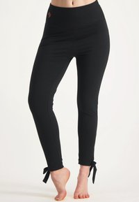 Svarta leggings med hög midja, med sid sömmar och dekorerande rosetter vid anklarna. Tillverkade av ett mjukt, stretchigt tyg.