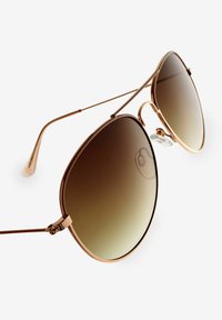 Gafas de sol de metal en color oro rosa con lentes ovalados de gran tamaño, tintado en degradado marrón, varillas finas y almohadillas nasales transparentes para mayor comodidad.