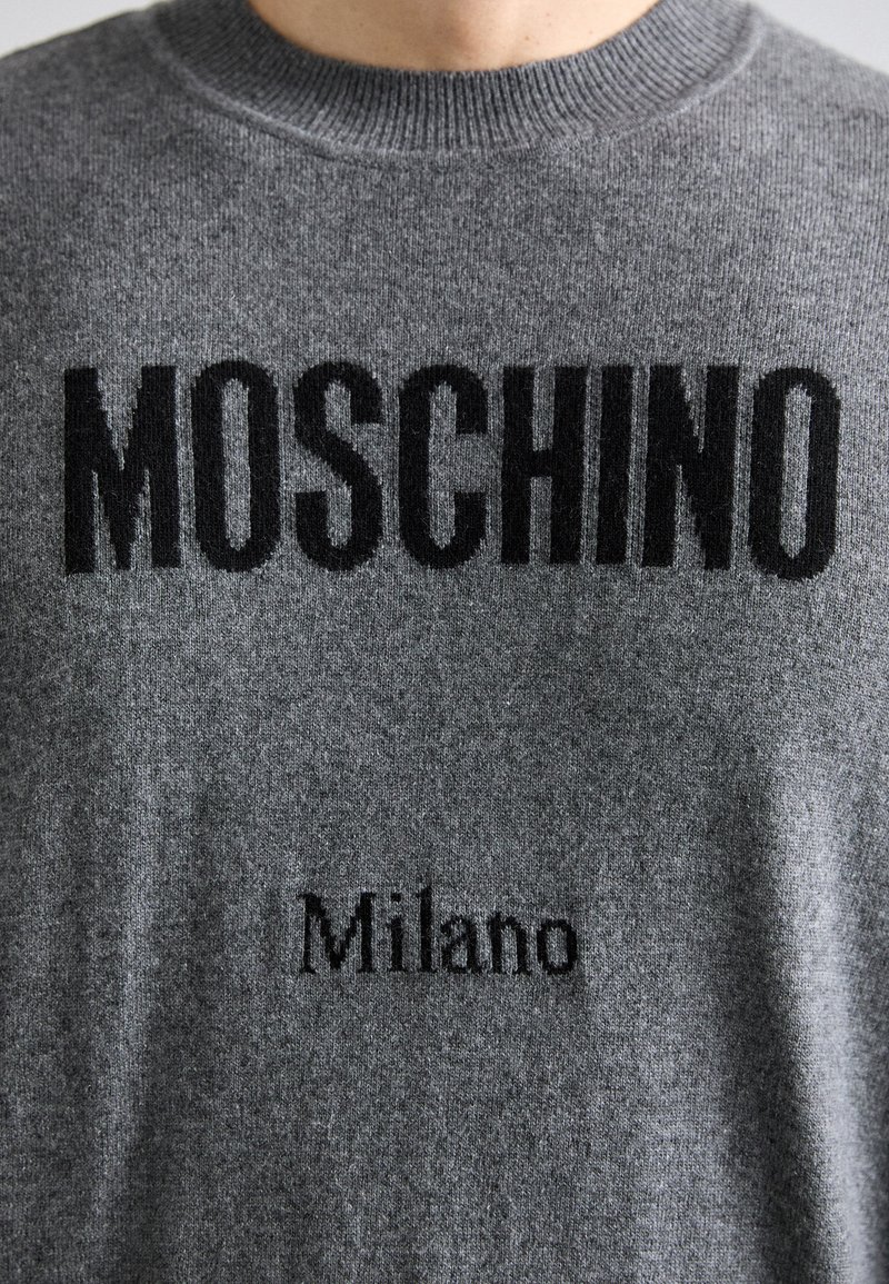 Grauer gestrickter Pullover mit "MOSCHINO" in fetten schwarzen Buchstaben und "Milano" in kleinerem Text. Weiche Textur und Rundhalsausschnitt-Design.