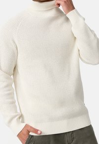 Pull à col roulé crème avec un motif tricoté texturé, poignets et ourlet côtelés. La coupe est décontractée, adaptée au superposition.