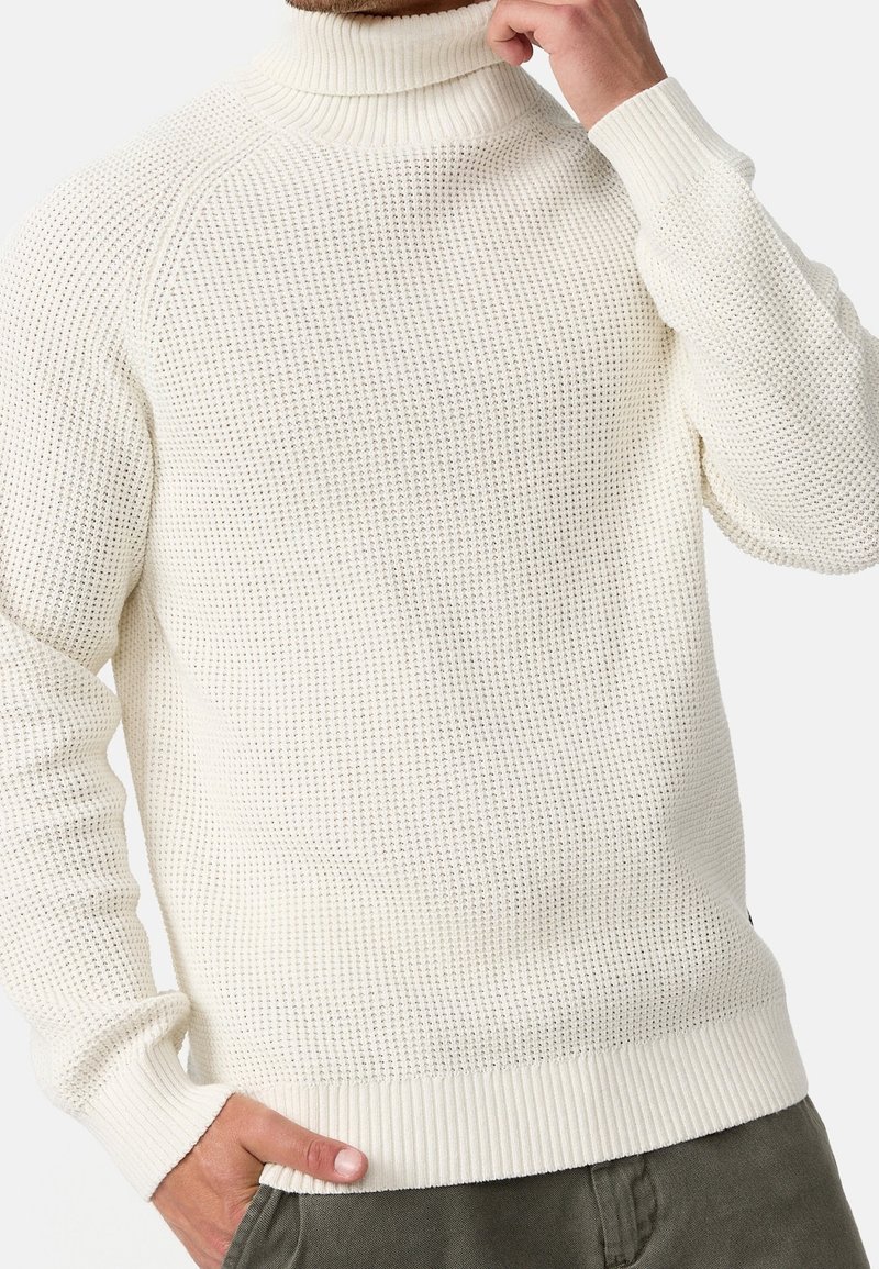 Pull à col roulé crème avec un motif tricoté texturé, poignets et ourlet côtelés. La coupe est décontractée, adaptée au superposition.