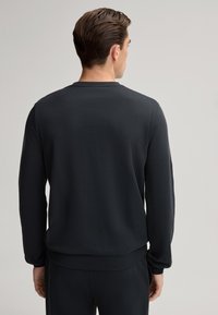 Zwarte sweatshirt van zacht materiaal. Heeft lange mouwen, een ronde halslijn en een losse pasvorm. Soepele textuur met een eenvoudig ontwerp.