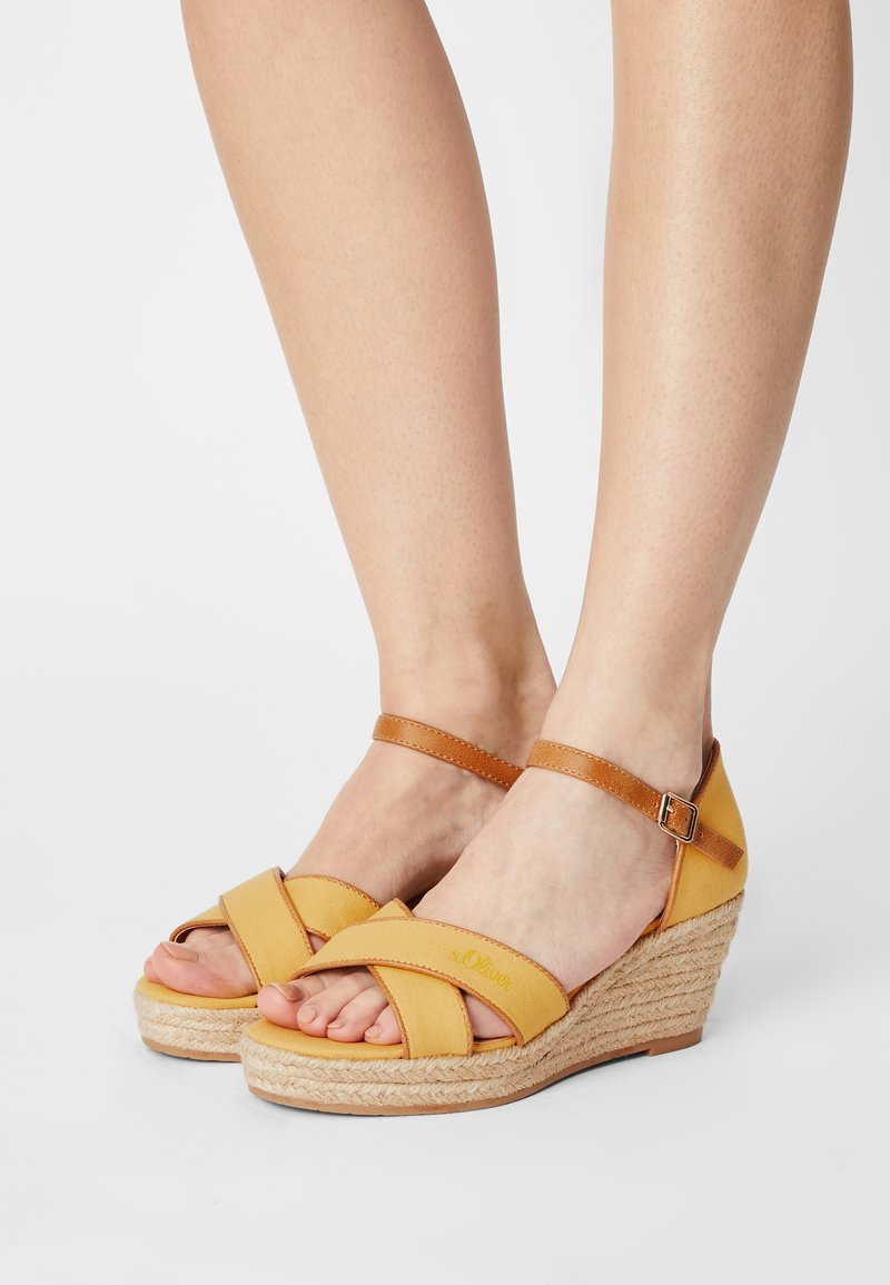 Yellow wedge sandals with crossed fabric straps, leather ankle strap, and woven jute platform. Features a low heel and open toe design.