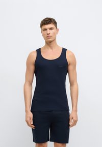 Námornícky modrý rebrovaný tielko s okrúhlym výstrihom a detailom loga na ľavej strane hrudníka. Kombinované s tmavými šortkami v rovnakom odtieni, minimalistický dizajn.