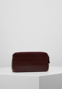 Burgundy tekonahka krokotiilinsuomuilla, jossa on tekstuuripinta, kultasävyinen ketjuakseli ja vetoketjukiinnitys. Kompakti suorakulmainen muoto.