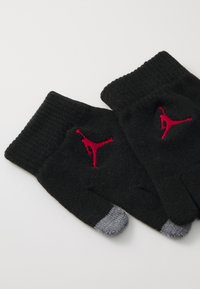 Black knitted gloves with red embroidered logo, featuring fingertip openings, and grey accent on tips for touchscreen use.