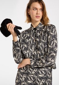 Košile s dlouhým rukávem v černo-bílém abstraktním vzoru, se límcem a zapínáním na knoflíky, s modelem, který drží černé rukavice.