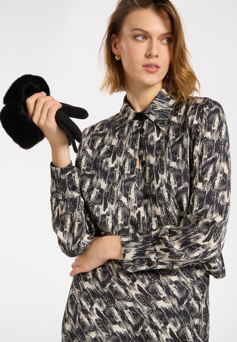 Košile s dlouhým rukávem v černo-bílém abstraktním vzoru, se límcem a zapínáním na knoflíky, s modelem, který drží černé rukavice.