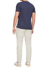 Navy blauw t-shirt met korte mouwen, gecombineerd met lichtbeige broek en witte sneakers. Het t-shirt heeft een ronde hals en minimale branding.