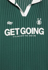 Zelená rebrovaná polokošeľa s bielym golierom. Obsahuje text "POĎME DO TOHO, JE TO VO VÁS A VO MNÁ" v tučnom bielom písmene a detail "1991".