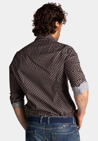 Patroon met een donkere blouse met een klein bloemenmotief, contrasterende manchetten en een opvallende kraag; de stof is soepel met een getailleerde pasvorm.