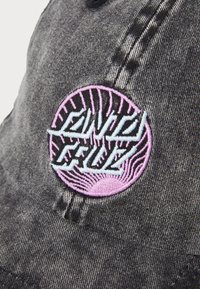 Zwarte denim pet met een rond geborduurd patch in roze en blauw met radialen en de tekst "Santa Cruz."