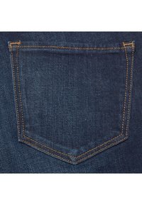 Detailní záběr na zadní kapsu modrých džínů s viditelným oranžovým prošíváním a texturou látky.