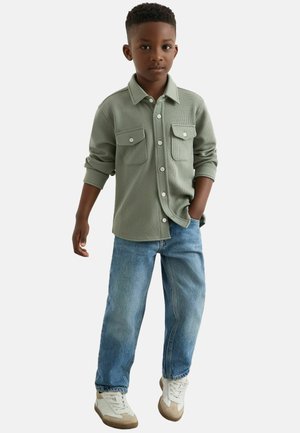 Grün kariertes Button-up-Hemd mit zwei Brusttaschen, kombiniert mit hellblauen Jeans und beigen Sneakern.