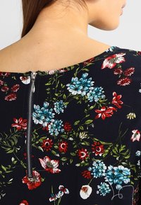 Abito floreale con sfondo blu navy e fiori rossi, blu e bianchi. Chiusura con zip sul retro e tessuto morbido con una superficie liscia.