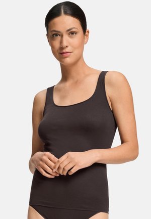 Woman with dark hair tied back wearing a sleeveless black tank top against a plain light background.