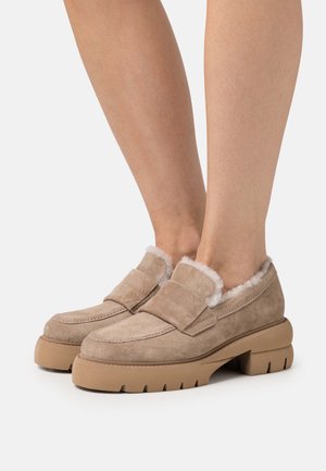 Beige Wildleder-slipper mit dicker, robuster Sohle. Ausgestattet mit einem samtigen Fellfutter und einem breiten Riemen über dem Obermaterial.