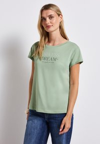 Světle zelené bavlněné tričko s kulatým výstřihem a krátkými rukávy, na přední straně s potiskem "NEKONEČNÝ SEN" v kontrastních barvách.