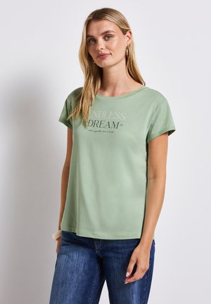 Camiseta de algodón verde claro con cuello redondo y mangas cortas que presenta el texto "SUEÑO INFINITO" impreso en el frente en colores contrastantes.