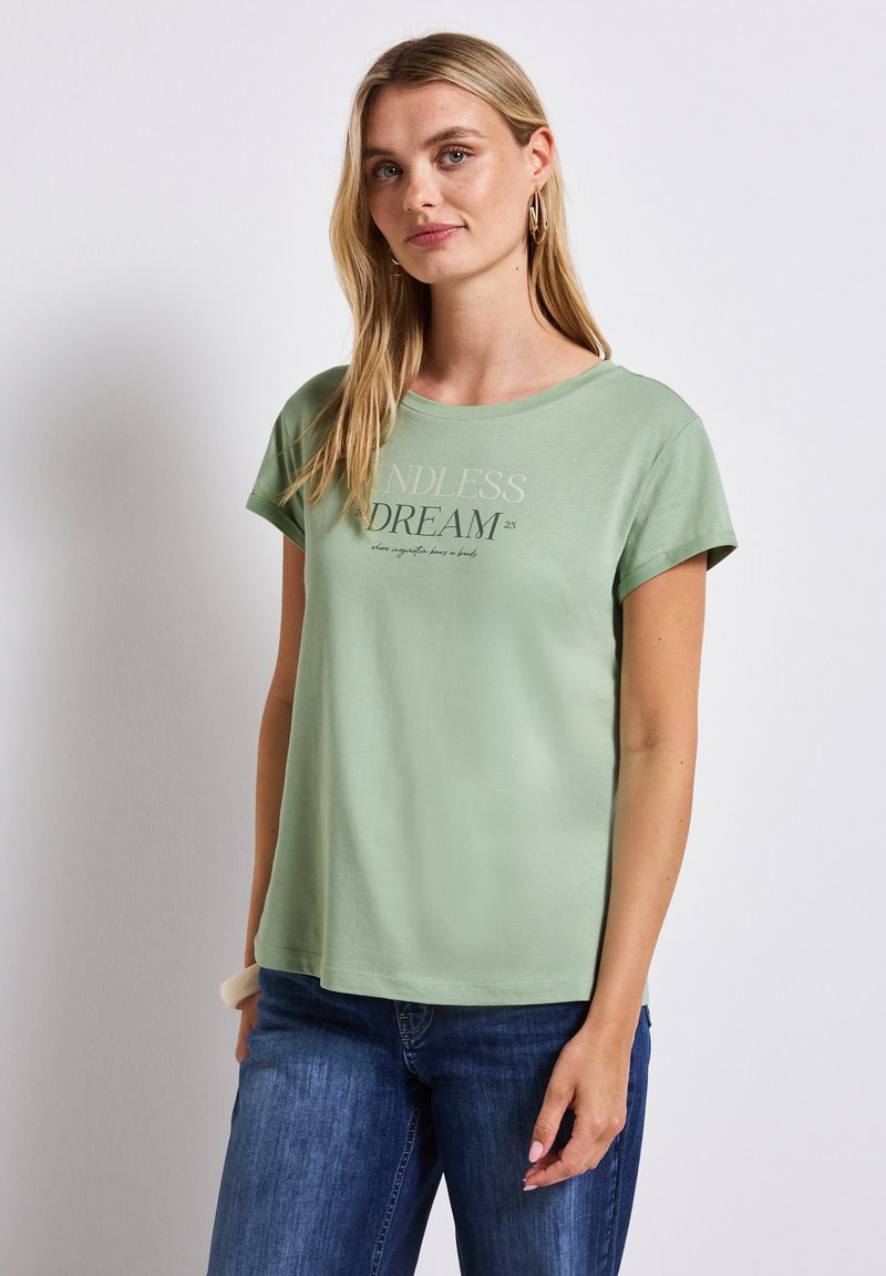 Světle zelené bavlněné tričko s kulatým výstřihem a krátkými rukávy, na přední straně s potiskem "NEKONEČNÝ SEN" v kontrastních barvách.