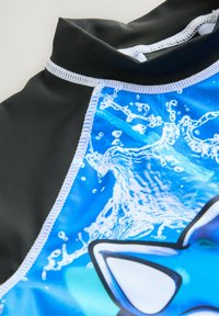 Maglietta da nuoto nera con colletto alto, caratterizzata da una grafica blu di schizzi d'acqua e una forma di pesce, arricchita da dettagli di cucitura bianca.