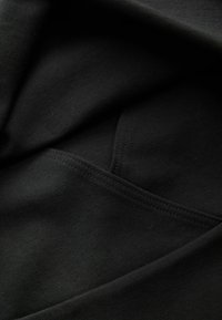 Schwarzer Stoff mit glatter Textur, sichtbaren Nähten und einem kleinen Taschendetail, das in das Design integriert ist.