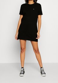 Svart t-shirt klänning i bomull med korta ärmar, rundad halsringning och en liten logotyp på bröstet. Matchad med svarta högklackade sneakers.