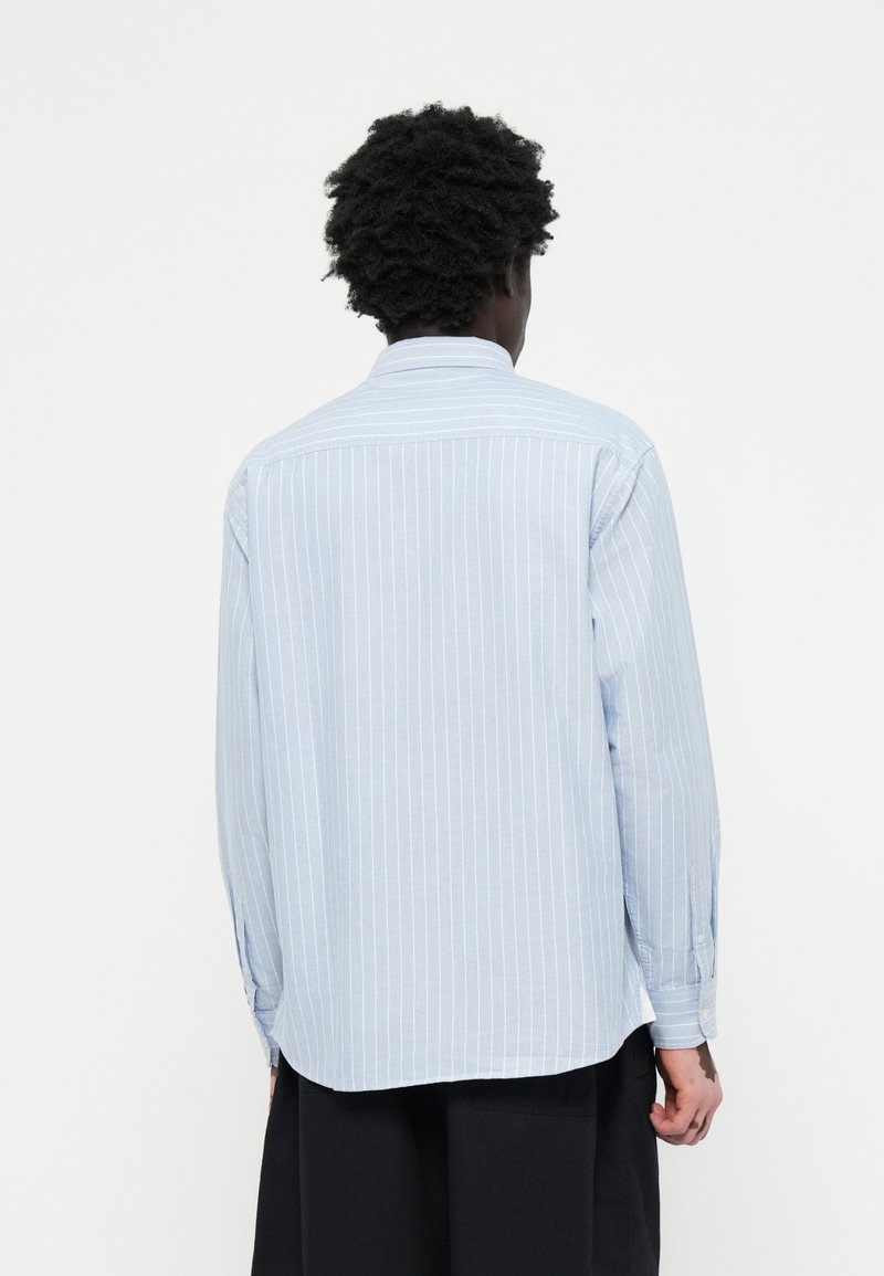 Chemise à manches longues bleu clair avec des rayures blanches verticales, poignets à boutons et col classique. Tissu doux avec une coupe décontractée.