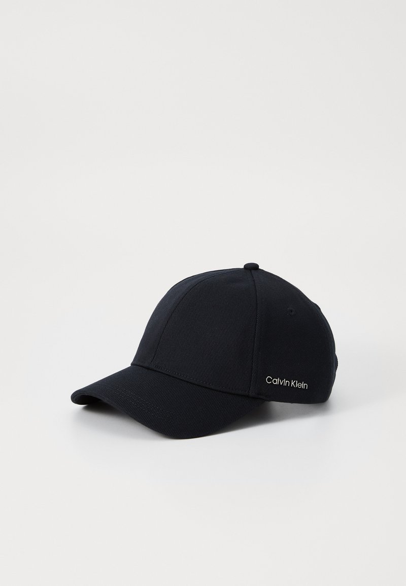 Black baseball cap made of textured fabric. Features a curved brim and small embroidered "Calvin Klein" logo on the side.