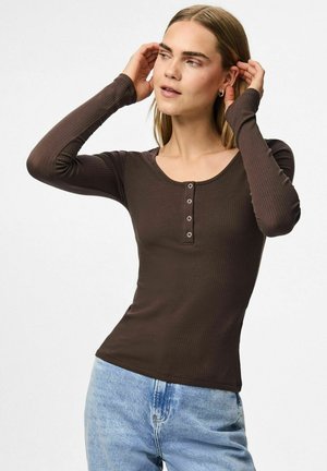 Bruine geribbelde lange mouw top met een ronde halslijn en een knoopsluiting van vijf knopen; aansluitend model in combinatie met lichtblauwe hoge taille jeans.