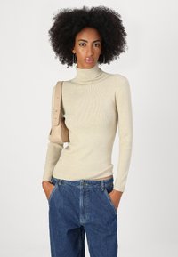 Beige ribbestr turtleneck genser med en tettsittende silhuett, kombinert med høyt liv blå denim jeans og en lys tan skulderveske.