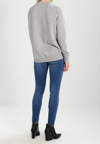 Šedá mikina s dlouhými rukávy, žebrovanými manžetami a lemem. V kombinaci s modrými skinny džíny a černými kotníkovými botami. Pohled na outfita zezadu.