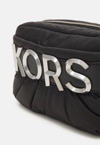 Borsa in nylon trapuntato nera con un prominente logo "KORS" in argento su un cinturino nero opaco, con dettaglio di chiusura con zip dorata.