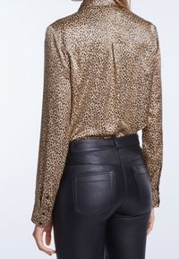 Leopardprint blouse met een glanzende, gestructureerde afwerking; heeft een kraag, lange mouwen en een rugnaadontwerp. Gecombineerd met zwarte leren broek.