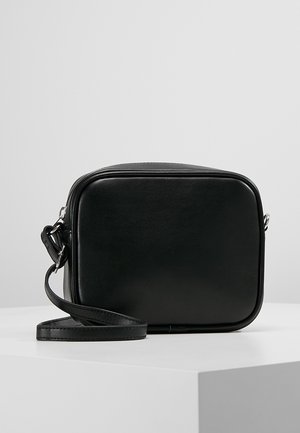 Sort rektangulær læder crossbody taske med afrundede kanter og justerbar rem, placeret på en hvid overflade mod en ensfarvet baggrund.