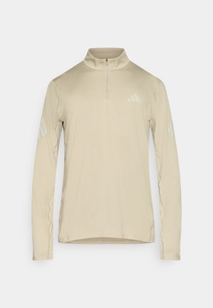Beige sporttop met lange mouwen en een rits aan de kraag. Voorzien van lichtgekleurde drie-strepen accenten op de schouders. Soepele textuur en nauwsluitend ontwerp.