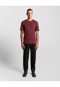 Vīnogu krāsas īsroku t-krekls ar apaļu apkakli un nelielu logotipu uz krūtīm, kopā ar melnām taisnajām biksēm un melniem zābakiem.