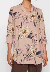 Blus med blommigt mönster i ljusrosa, v-ringning, trekvartslånga ärmar och knapprad vid halsringningen. Tillverkad av mjukt, lätt tyg.