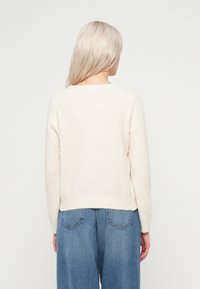 Φουσκωτό κρεμ πουλόβερ με στρογγυλή λαιμόκοψη, μακριά μανίκια και ριγωτό στρίφωμα, συνδυασμένο με ελαφρώς φαρδιά ανοιχτό μπλε τζιν.