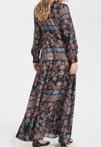 Robe maxi en tissu noir avec des motifs floraux en rouge, bleu et blanc. Elle présente des manches longues, un col haut et une silhouette fluide.