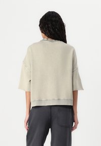 Ljusgrå, överdimensionerad sweatshirt med korta ärmar, rundad nederkant och synliga sömmar. Matchad med mörkgrå byxor med en bakficka.