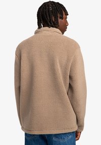 Beige fleece pullover jacket with a high collar and textured fabric. Features long sleeves and a relaxed fit, viewed from the back.