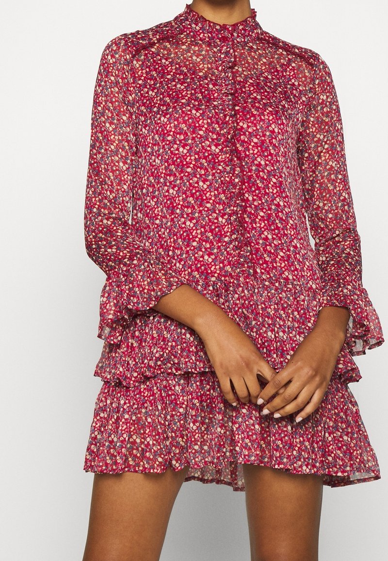 Floral-printed dress in sheer fabric, featuring a high neck, long sleeves, tiered ruffles, and shades of red, pink, and cream.