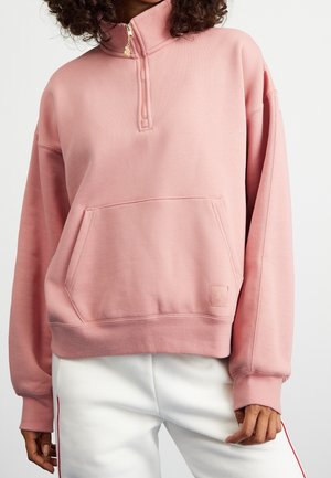 Sweatshirt rose clair avec un col haut et une demi-fermeture éclair. Dispose d'une poche kangourou à l'avant et de poignets côtelés. Matériau doux et texturé.