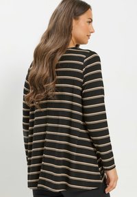 Camiseta negra de manga larga con finas rayas horizontales beiges, textura acanalada y un corte holgado con aberturas laterales en el dobladillo.